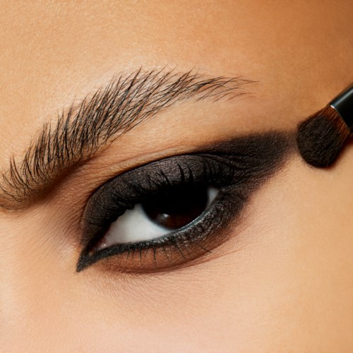 Närbild av ett öga med mörk ögonskugga och en makeuplbrush som applicerar svart ögonskugga.