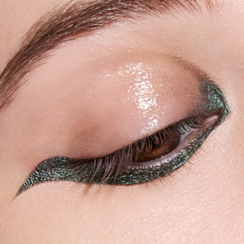 Läheinen suljetusta silmästä, jossa on glitterinen teal- ja musta silmämeikki ja luonnolliset kulmakarvat.