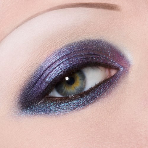 Närbild av ett mänskligt öga med livfull lila och blå ögonskugga och svart eyeliner.