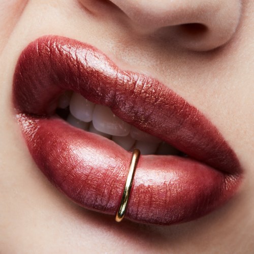 Close-up of lips with red lipstick, a small gold ring on the lower lip, and teeth showing.