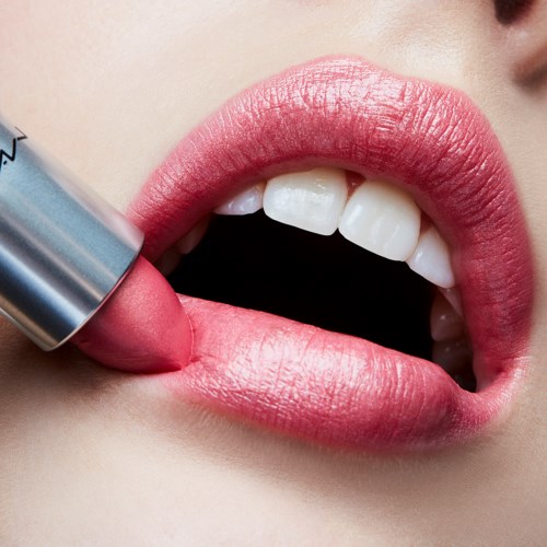 A person applies pink lip balm on lips, with teeth and face close up. The lips look smooth and shiny.