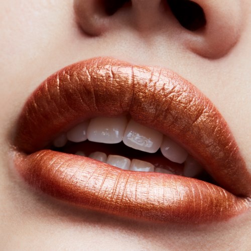 Close-up of lips with metallic gold lipstick and visible teeth beneath.