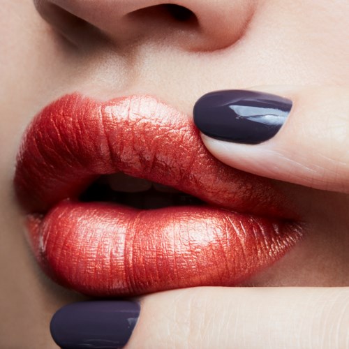 Close-up of lips with red and shiny lipstick, and a finger with dark nail polish touching lips.