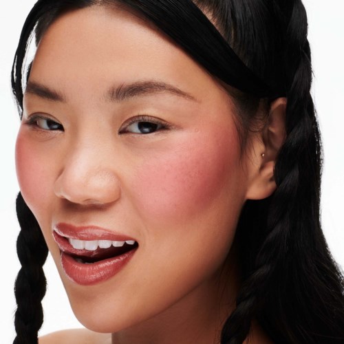 A woman with braided hair, smiling with her mouth open, showing teeth, and having rosy cheeks.