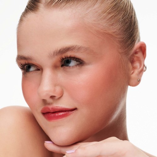 A young woman with blonde hair tied back, blue eyes, and a gentle smile, looking to the side. Clear skin.