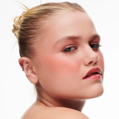 A woman with blonde hair in a bun, looking over her shoulder with a slight smile.