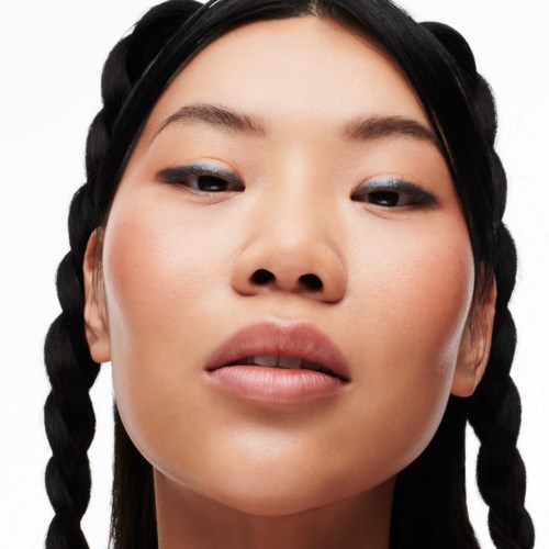 Eine Frau mit geflochtenen Haaren, leichtem Make-up und einem selbstsicheren Blick schaut direkt in die Kamera.