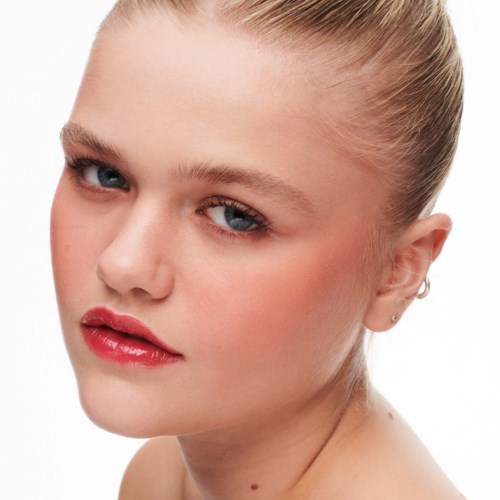 A young woman with blonde hair tied back, blue eyes, and wearing red lipstick.