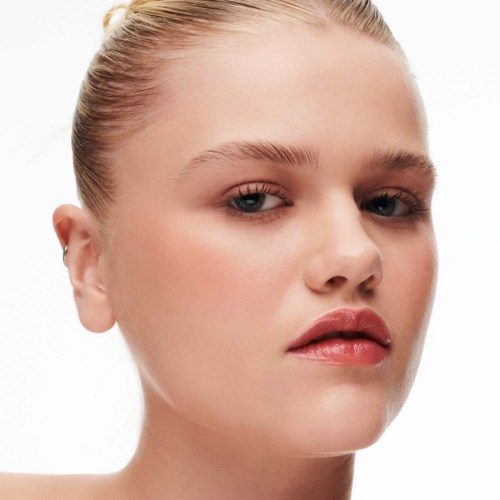 A woman with smooth skin, light makeup, and blonde hair tied back, looking confidently at the camera.