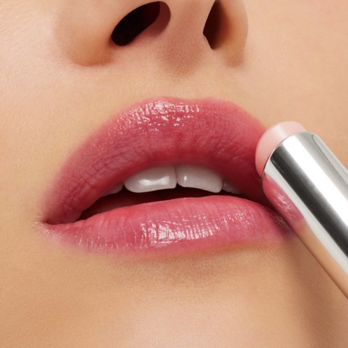 Close-up of lips being touched with pink lipstick from a tube.
