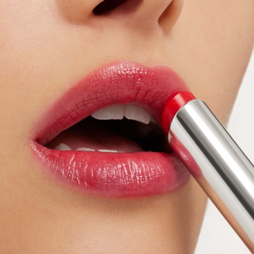 A person applies red lipstick on lips, showing close-up of mouth and part of nose.