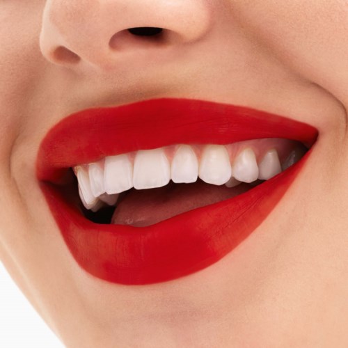 Eine Person lächelt, zeigt weiße Zähne und trägt roten Lippenstift.