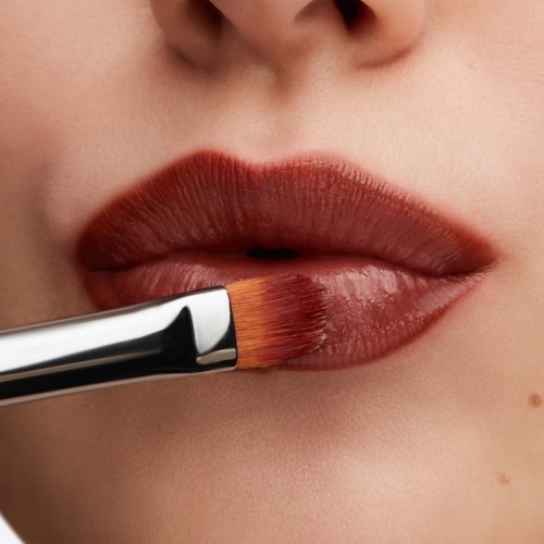 Närbild av läppar som målas med en pensel, visar detaljerad makeup-applikation.