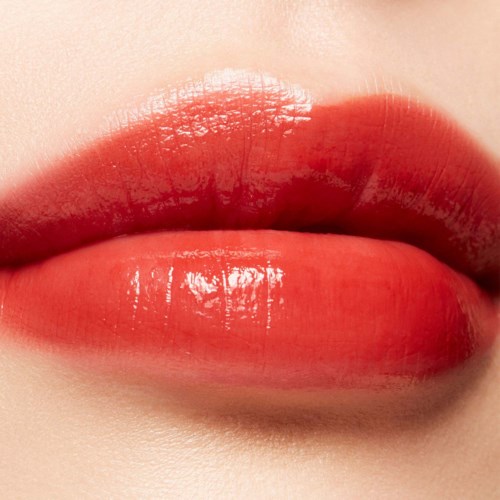 Close-up of lips with shiny, red lipstick, showing smooth skin and natural lip shape.