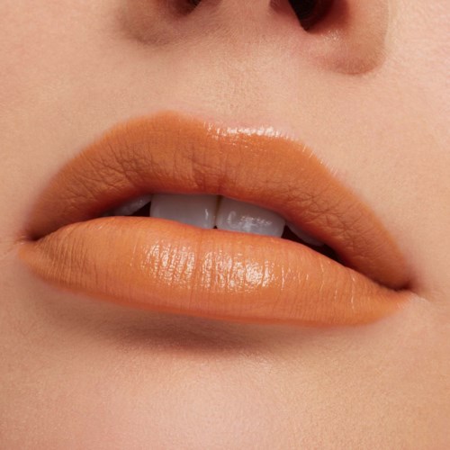 Close-up of lips with shiny peach-colored lipstick and slightly parted teeth.
