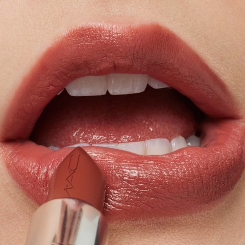 A person applying nude lipstick to lips, showing teeth and a tongue in a close-up.