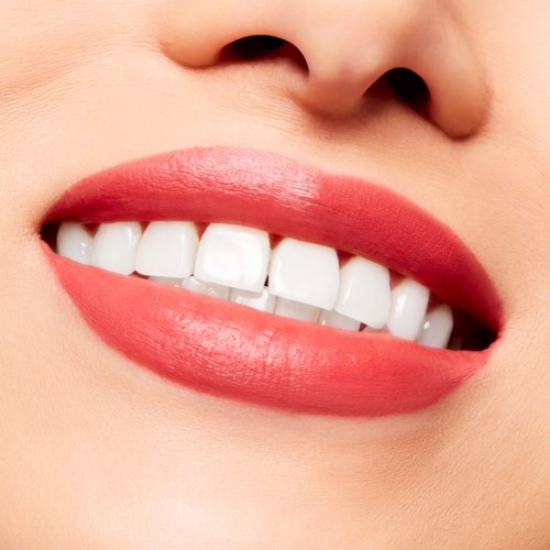 Close-up of a person’s smiling mouth showing white teeth and pink lips.