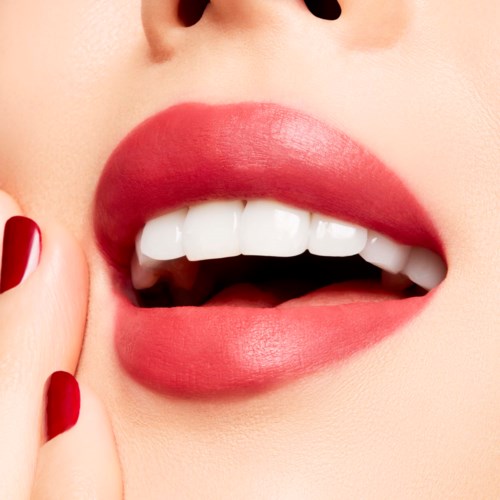 Close-up of lips with bright red lipstick and white teeth, part of face with finger touching cheek.