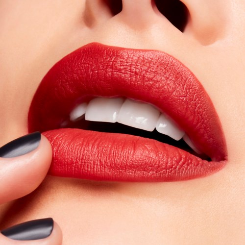 Close-up of lips with red lipstick, partly open, showing teeth, and a finger near the lips.