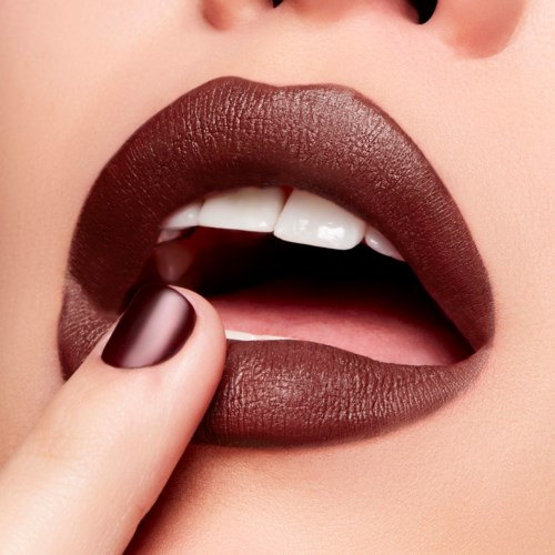 Close-up of lips with dark lipstick, showing a finger near the mouth, suggesting contemplation or silence.