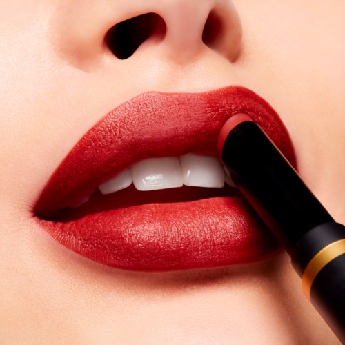 A person applying red lipstick to their lips, close-up on mouth, showing teeth and part of nose.