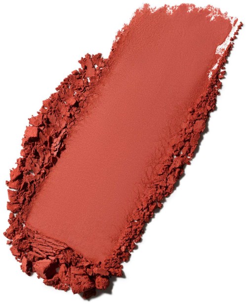 A rectangular coral-colored makeup blush or powder surrounded by crushed powder on white background.