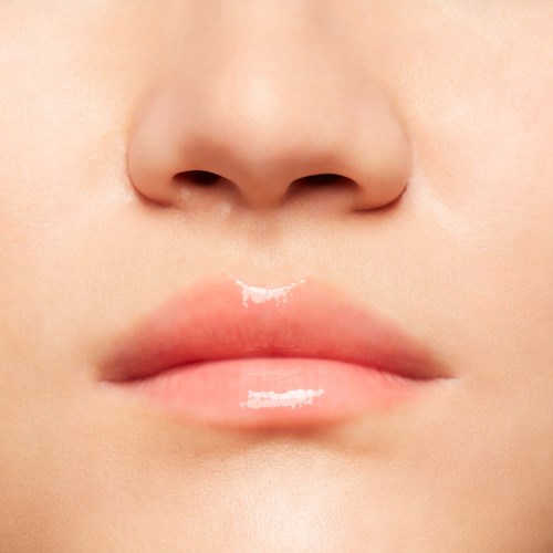 Close-up of lips with shiny gloss, part of a face, soft skin, small nose, light skin tone.