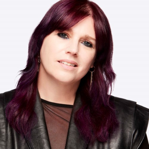 A woman with dark purple hair, wearing a black leather jacket, smiling slightly against a white background.