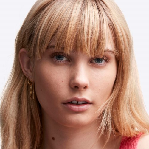 A young woman with blonde hair and blue eyes looks directly at the camera with a neutral expression.