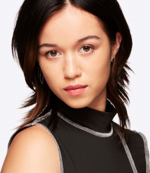 A young woman with dark hair, wearing a black sleeveless top, looking directly at the camera.