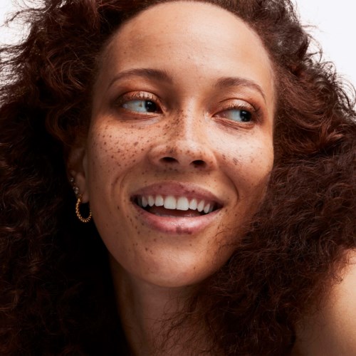 A woman with curly hair, freckled face, smiling and looking to the side.