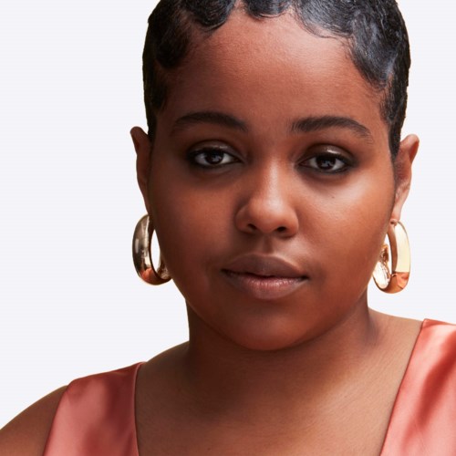 A woman with short hair wearing large earrings and a satin top, looking calmly at the camera.