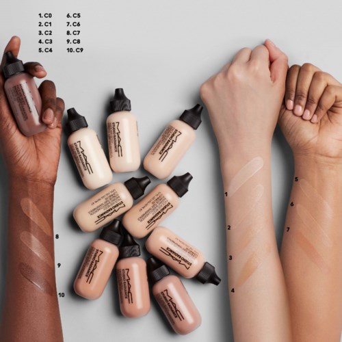 Multiple bottles of foundation with swatches on arms showing different shades. Text listing shade codes on the top left corner.