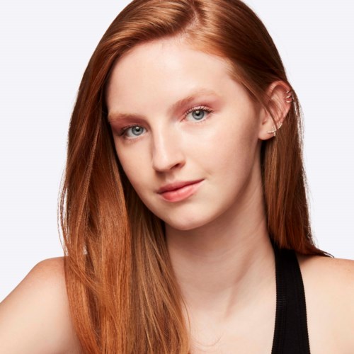 A young woman with long red hair, blue eyes, and a slight smile. She wears a black sleeveless top.