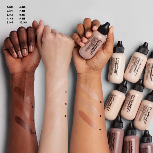 Three arms show different skin tones with swatches of foundation shades applied, alongside several bottles of foundation. Sample labels are numbered.