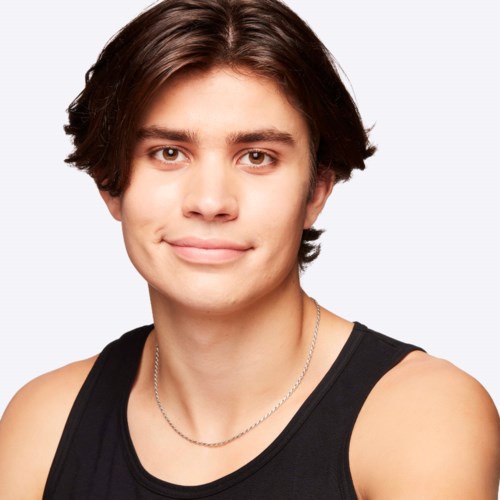 A young man with medium-length brown hair, wearing a black tank top and a silver chain, smiling softly.