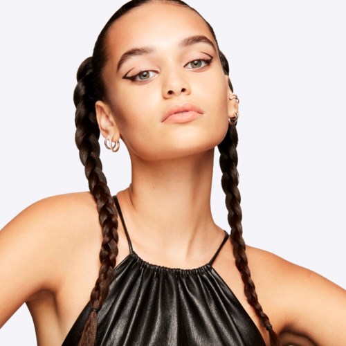 A woman with braided hair, makeup, and earrings wearing a shiny black top with arm holes.