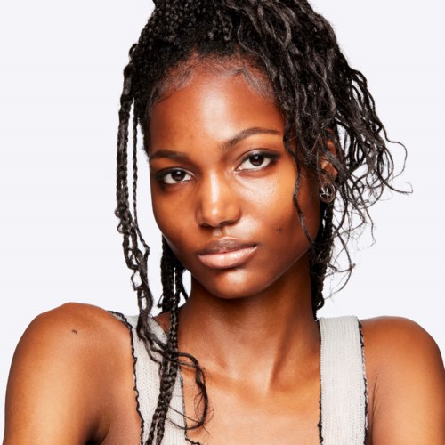 A young woman with dark, curly hair and a serious expression wears a sleeveless top.