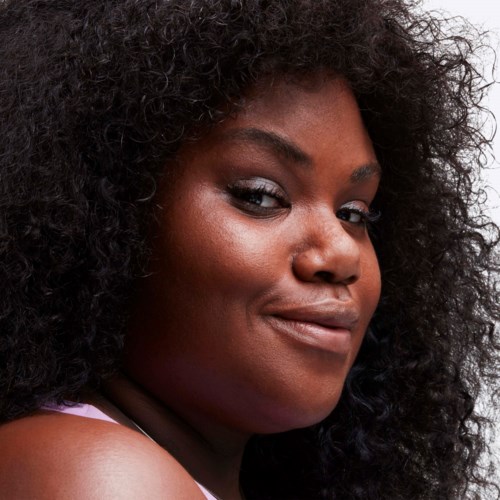 A woman with big, curly black hair, dark skin, and a confident smile, looking over her shoulder.