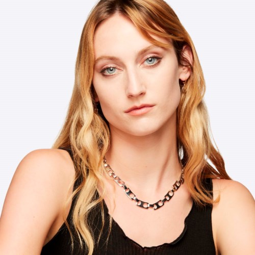 A young woman with blonde hair, blue eyes, wearing a black top and a silver chain necklace.