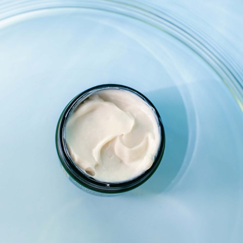 A jar of creamy white lotion floats on water with gentle ripples around it.