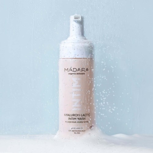 A bottle of intimate wash with foam around it, labeled Madara organic skincare, on a light background.