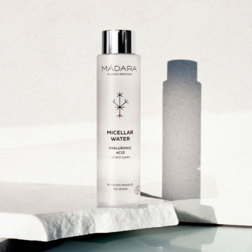 A white bottle labeled Madara Micellar Water, with a silver cap, standing on a textured surface.