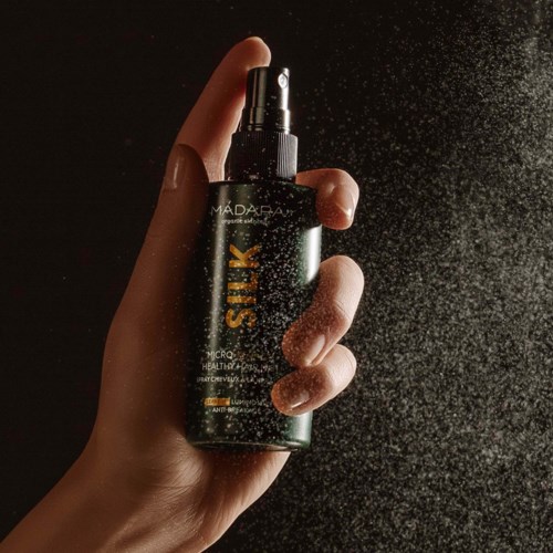A hand sprays mist from a black pack labeled 'SILK' against a dark background.