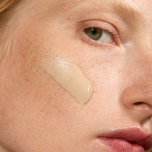 Close-up of a woman's face with foundation applied on the cheek and skin showing freckles.