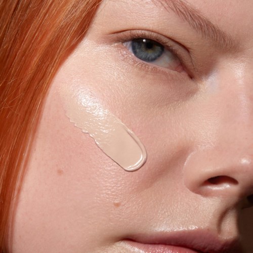 Close-up of a woman's face with a drop of skin cream on her cheek.