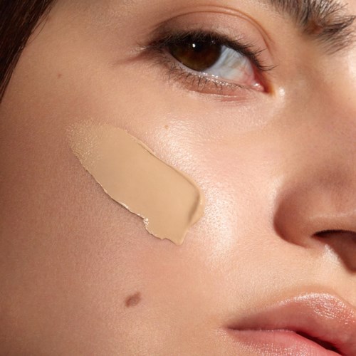 A woman has a beige makeup patch on her cheek near her nose and lips, with smooth skin and visible eye details.