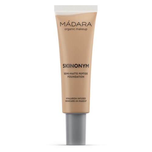 A beige tube of foundation labeled 'MÁDARA' with black text, indicating it's an organic, semi-matte, hyaluronic-infused product.