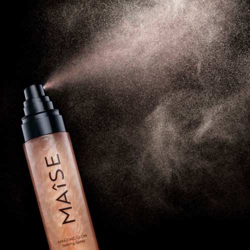 Eine Sprühflasche versprüht feinen Nebel von Setting Spray mit der Aufschrift 'MAISE' vor schwarzem Hintergrund.