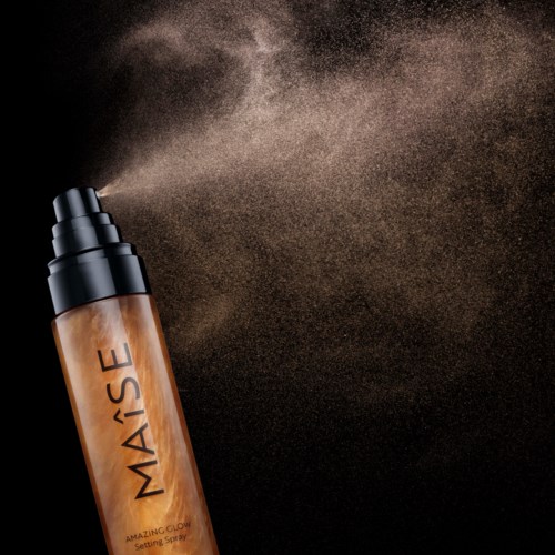Eine braune Sprühflasche versprüht ein feines Setting-Spray gegen einen schwarzen Hintergrund.